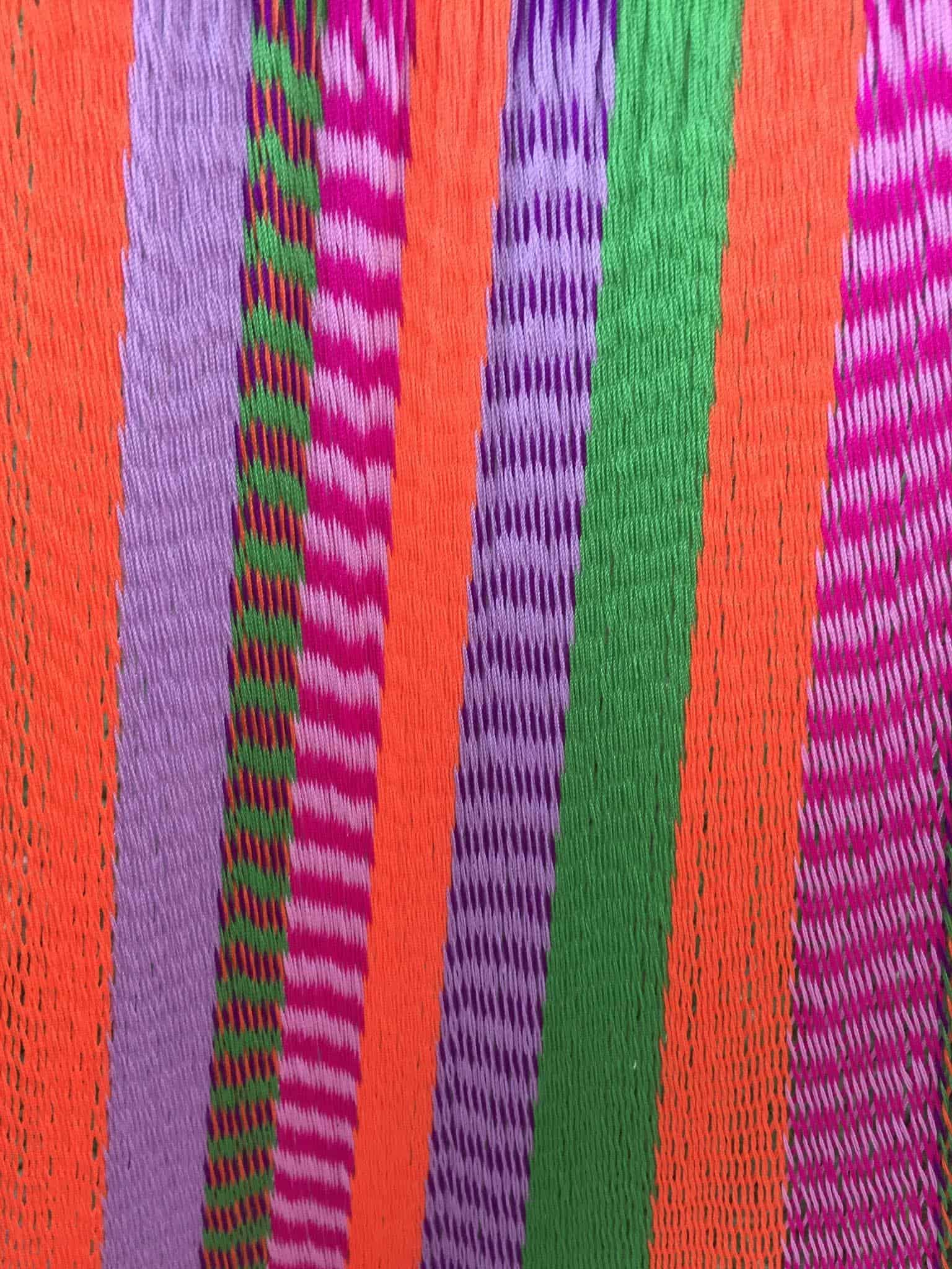 Close-up of the bright, colorful hammock featuring vertical stripes in neon orange, pink, green, and purple.