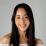 A portrait of a smiling adult woman in a white top, captured in a studio setting.