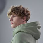 Portrait of a man with curly hair wearing a green hoodie, captured in a studio setting.