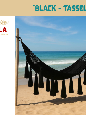 Black Hammock with Large Tassels on a sunny beach. Stylish, hand-woven hammock in solid black for a modern and chic outdoor retreat. Ideal for garden, patio, or coastal decor.