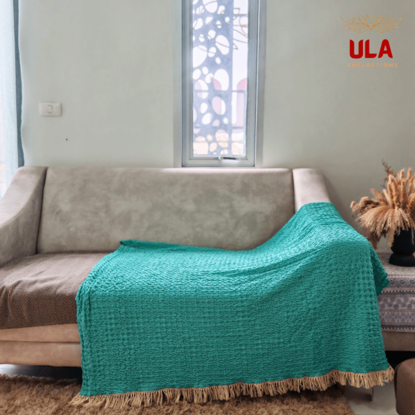 Full coverage turquoise ruffle throw blanket with tassels draped over a neutral sofa