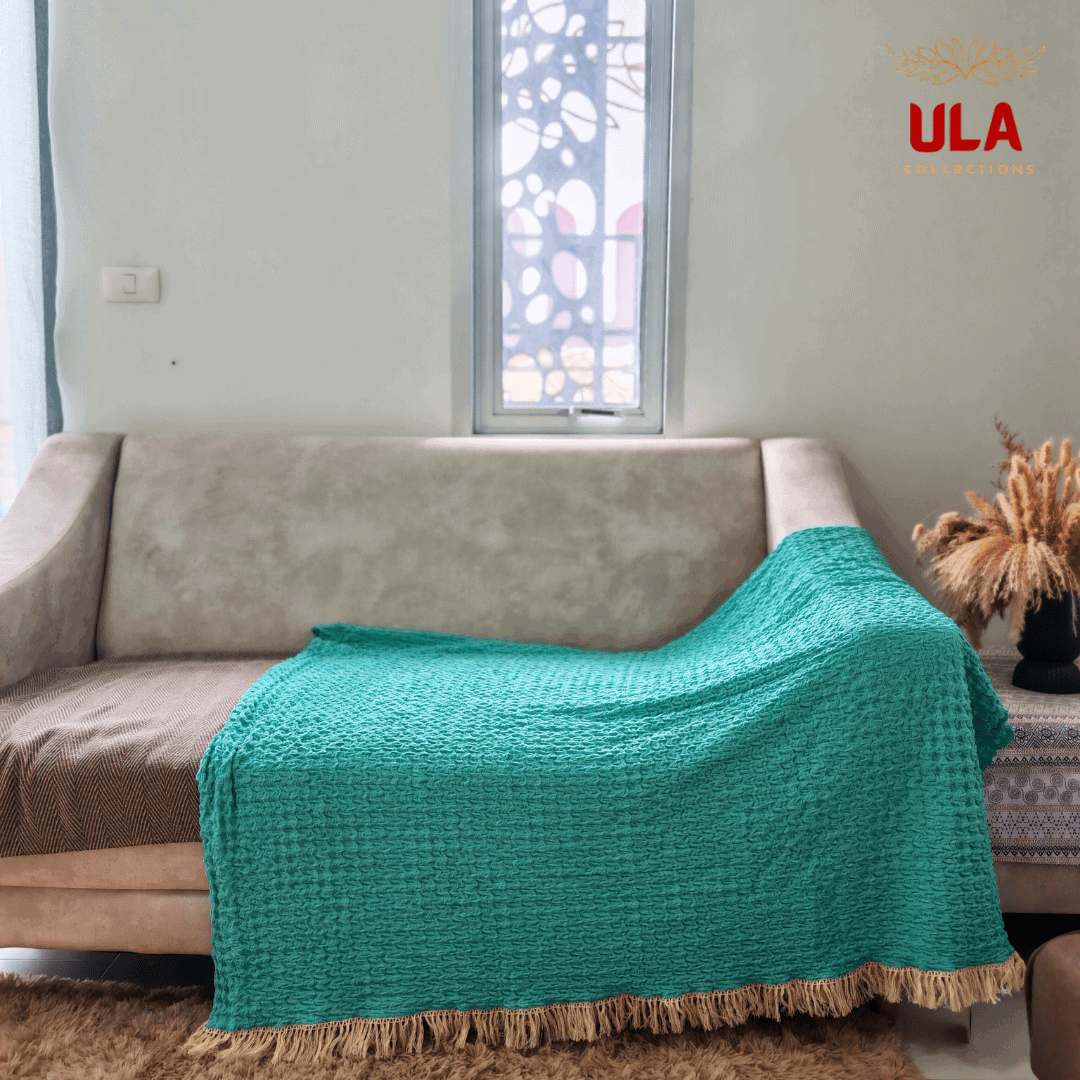 Full coverage turquoise ruffle throw blanket with tassels draped over a neutral sofa